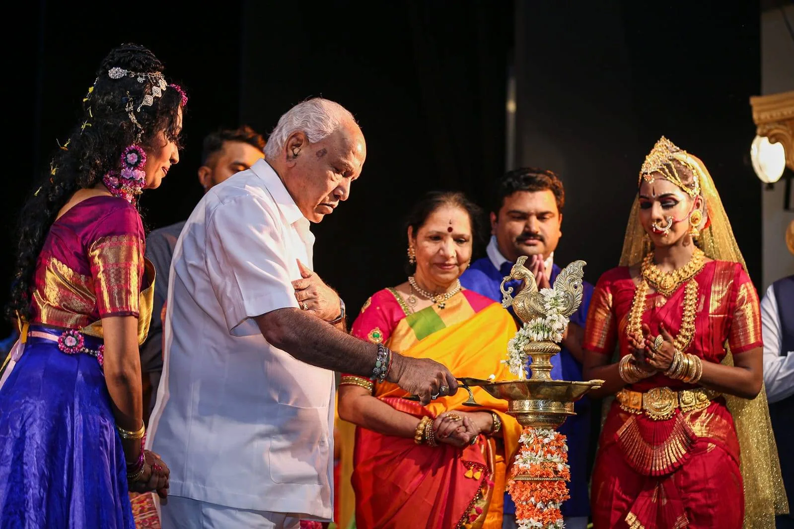 Former Karnataka Chief Minister B.S. Yediyurappa lighting the ceremonial brass lamp alongside costumed dancers